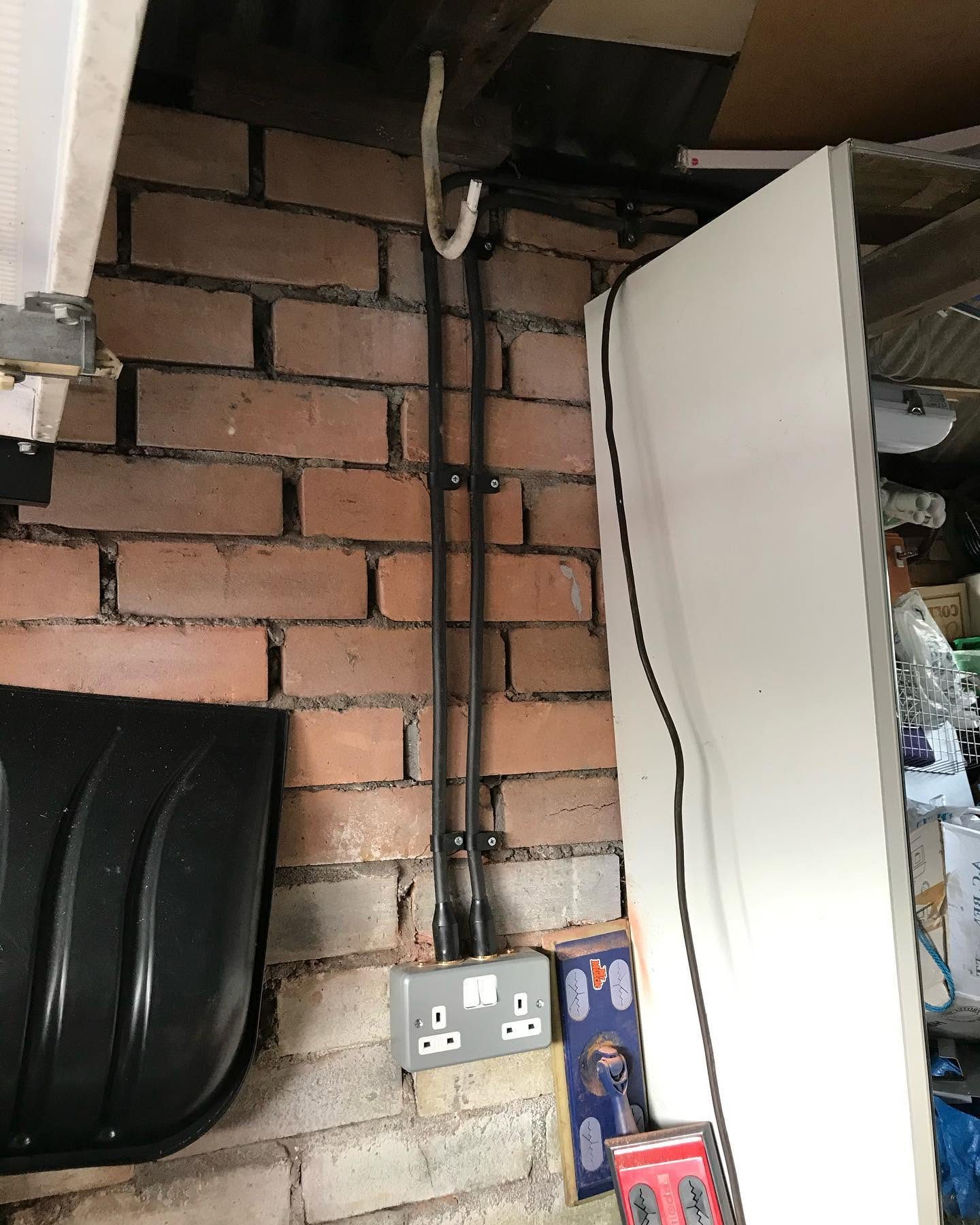 Surface conduit, cabling and double socket installed in a brick-walled utility area