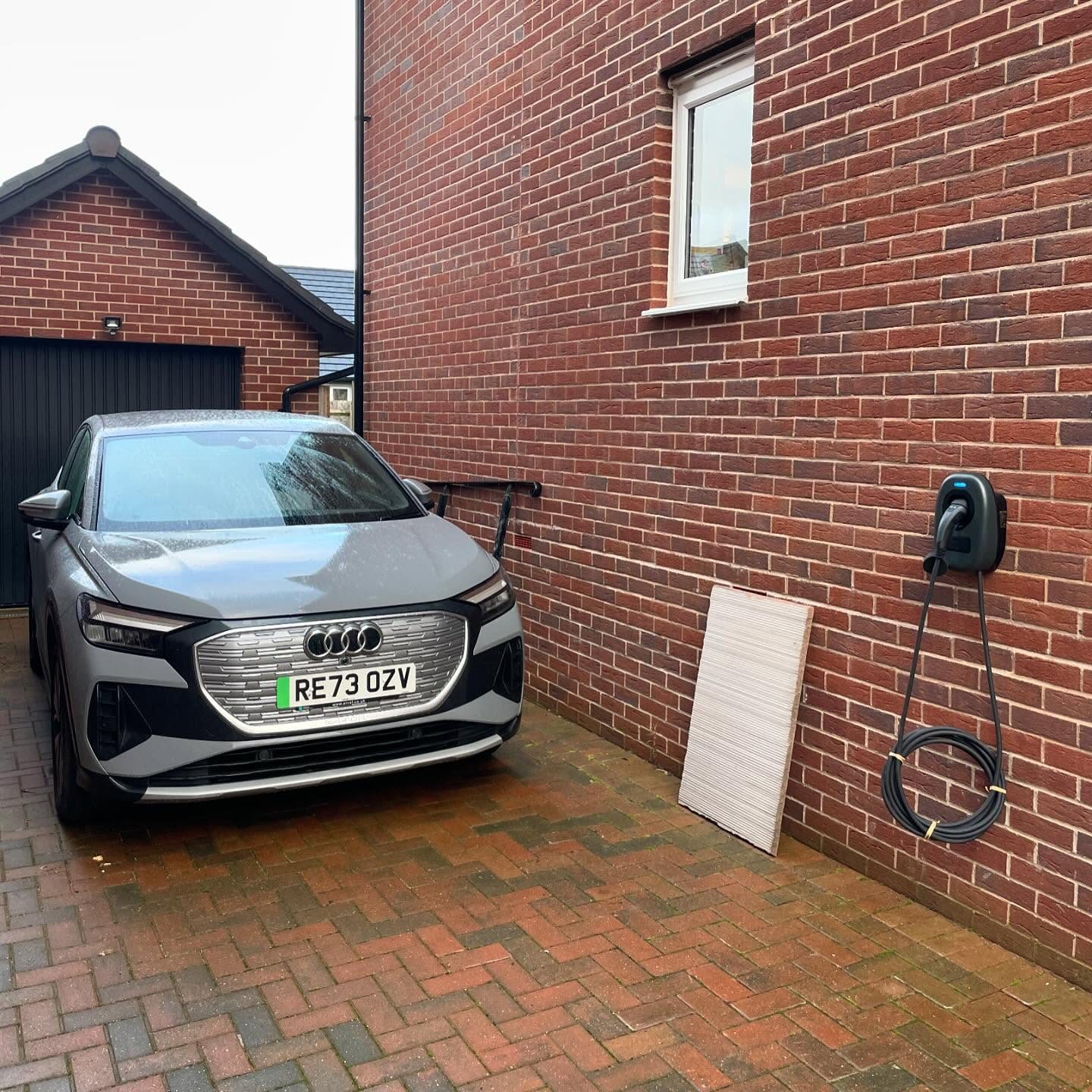Electric car parked beside a wall-mounted home EV charger on a brick house
